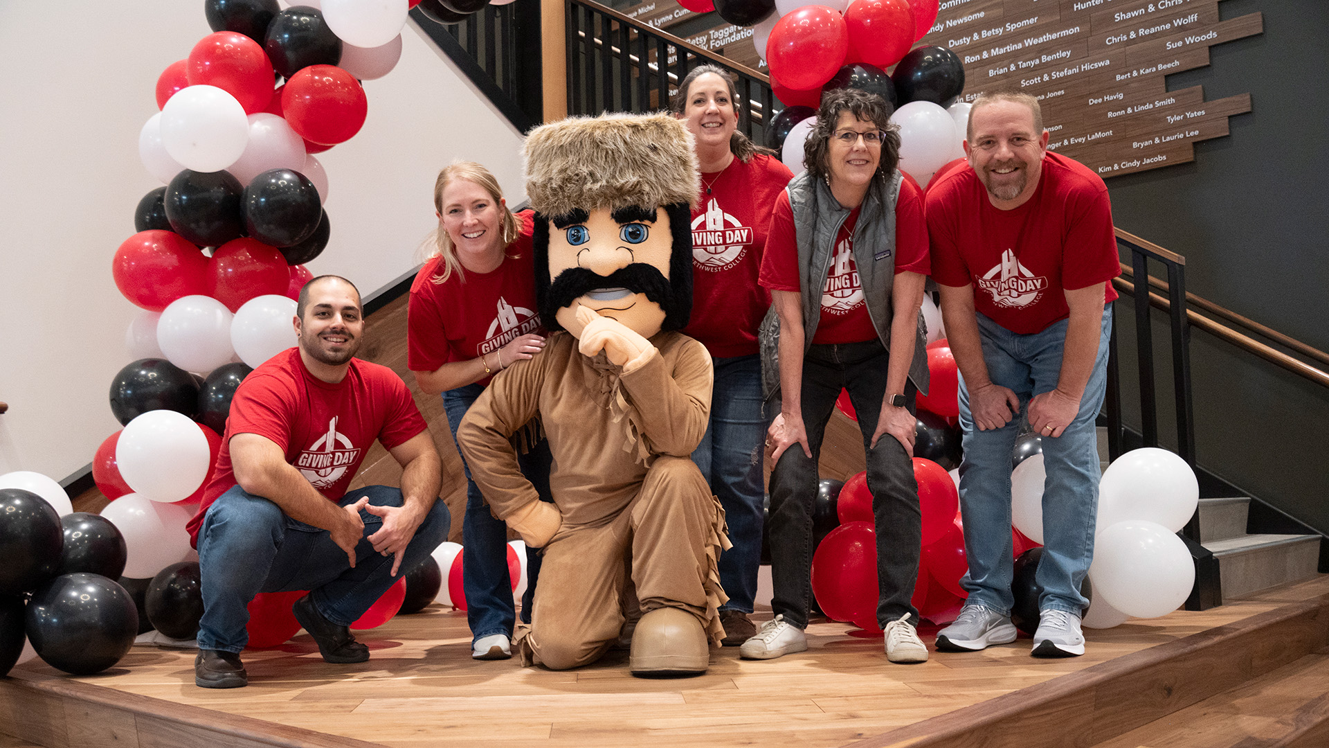 A group of college employees posing with the Trapper mascot in front of a balloon arch
